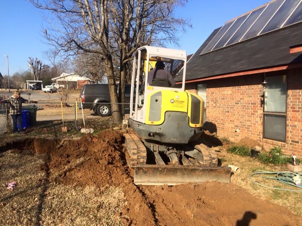 Mini excavator digging a trench beside a brick home