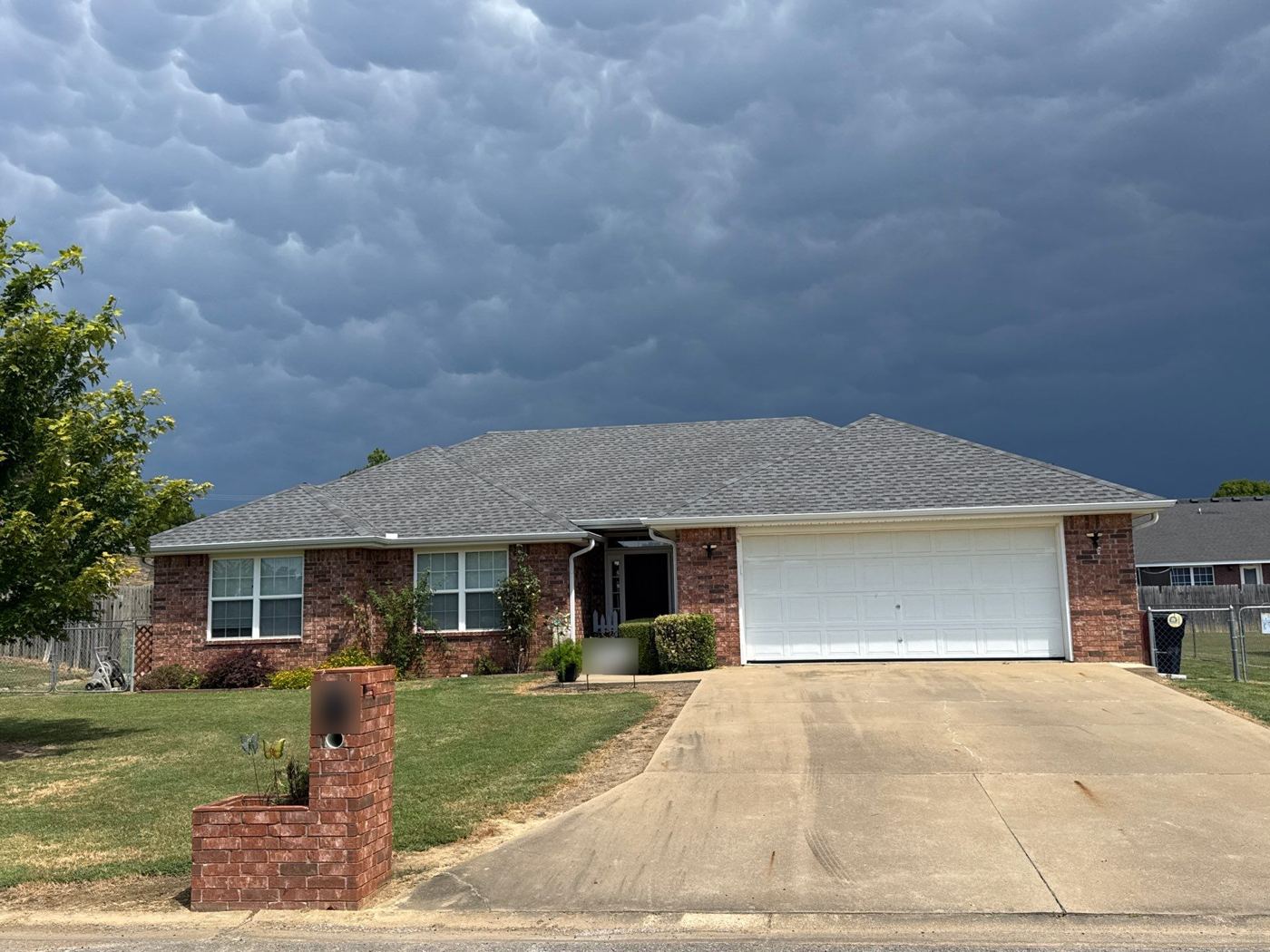 Brick home with a new gray shingle roof under storm clouds